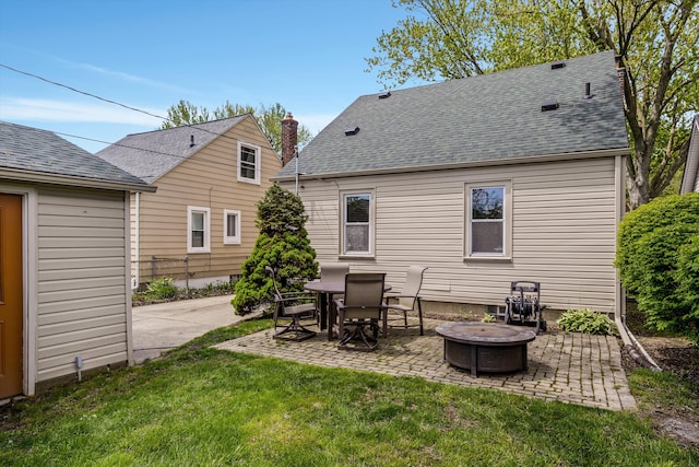 rear view of house featuring a fire pit, a patio, a yard, and a shingled roof