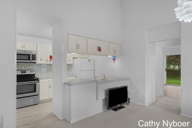 kitchen featuring stainless steel appliances, a sink, backsplash, white cabinetry, and light countertops