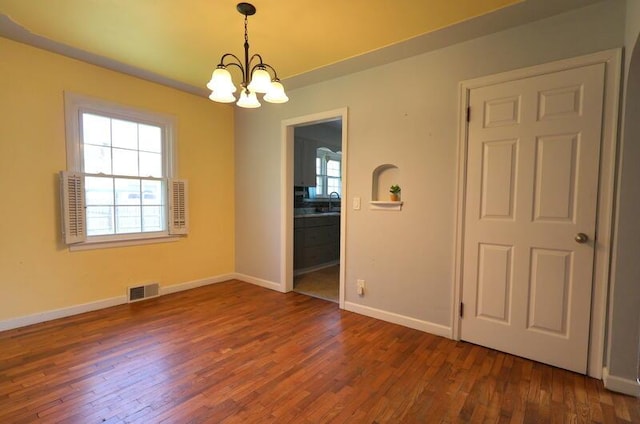 unfurnished room with a chandelier, wood finished floors, baseboards, and a sink