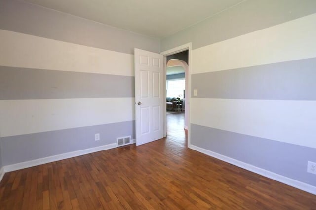unfurnished room featuring arched walkways, wood finished floors, and baseboards