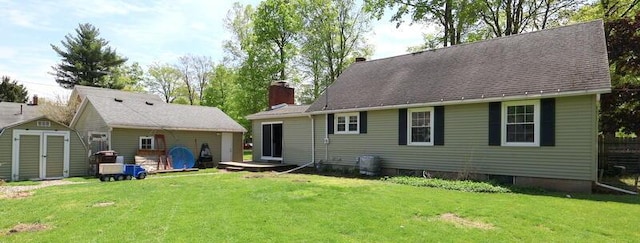 back of house featuring a storage unit, an outdoor structure, a chimney, and a lawn
