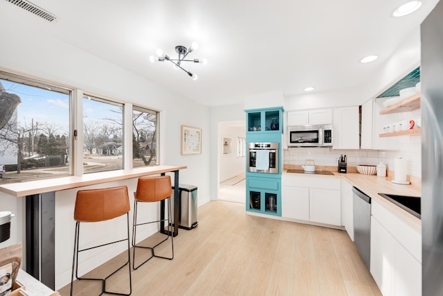 620 N Dr, New Buffalo, MI 49117 - kitchen with stainless steel appliances, tasteful backsplash, open shelves, light wood-type flooring, and visible vents