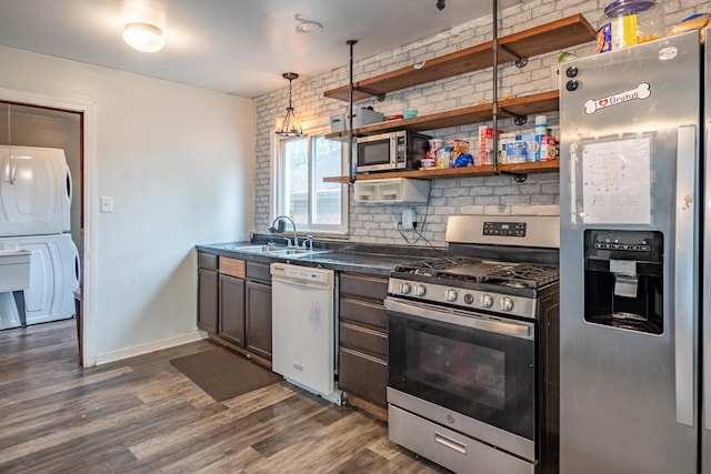 kitchen featuring stainless steel appliances, stacked washer / dryer, a sink, dark countertops, and dark wood-style floors