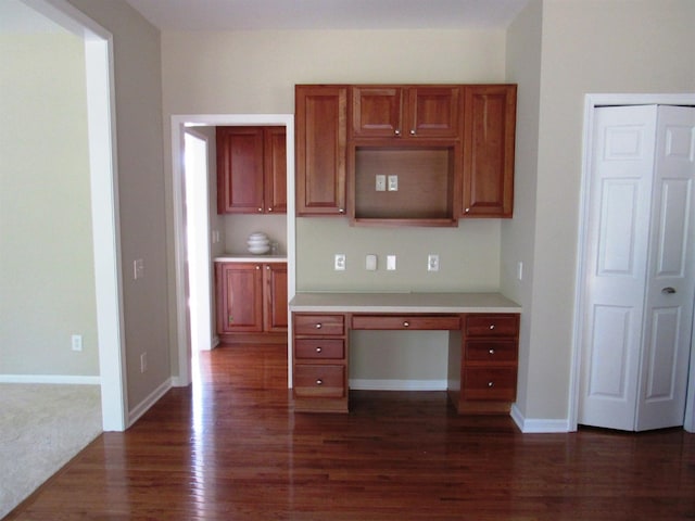 kitchen featuring light countertops, built in study area, dark wood-type flooring, and baseboards