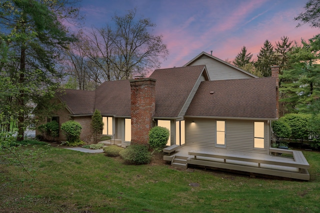 back of house with a chimney, a lawn, a wooden deck, and roof with shingles