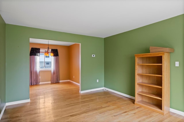 spare room featuring a chandelier, wood finished floors, and baseboards
