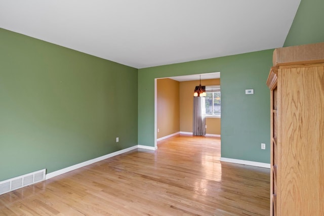 empty room with a chandelier, light wood-type flooring, and baseboards