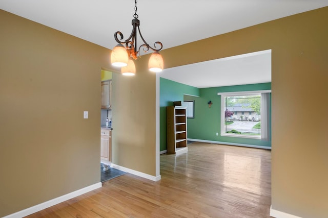 unfurnished room featuring light wood finished floors, a chandelier, and baseboards