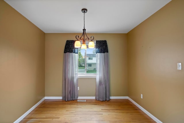 spare room with a chandelier, light wood finished floors, and baseboards