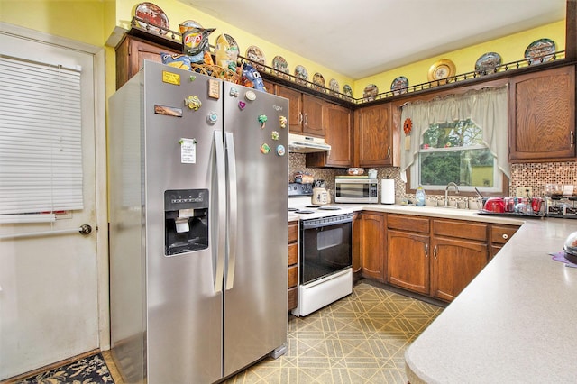 kitchen featuring appliances with stainless steel finishes, backsplash, under cabinet range hood, light countertops, and a sink