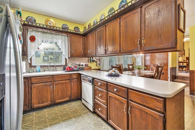 kitchen with white dishwasher, stainless steel fridge, a peninsula, light countertops, and tasteful backsplash