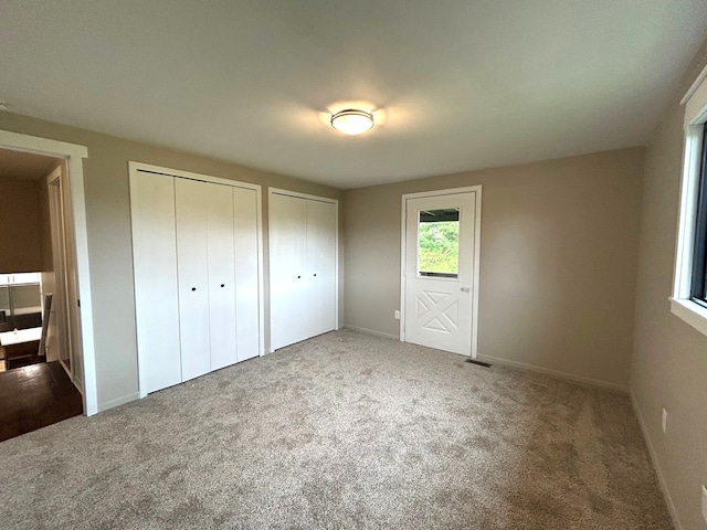 unfurnished bedroom with two closets, carpet, and baseboards