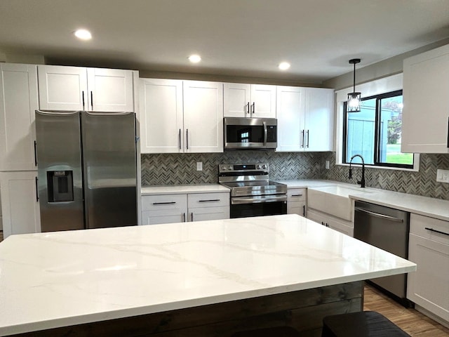 kitchen featuring appliances with stainless steel finishes, a sink, light stone counters, tasteful backsplash, and decorative light fixtures