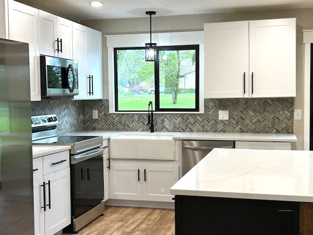 kitchen with stainless steel appliances, a sink, light wood-style flooring, white cabinets, and decorative backsplash