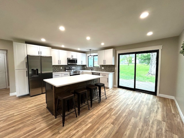 kitchen with appliances with stainless steel finishes, a sink, tasteful backsplash, baseboards, and light wood-style floors