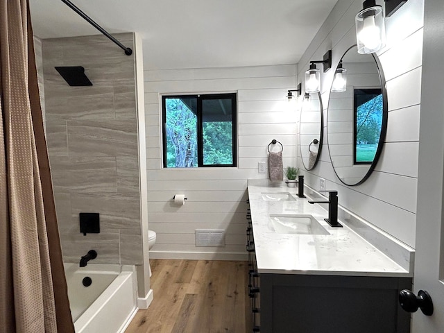 bathroom featuring wood finished floors, toilet, double vanity, and shower / bath combo