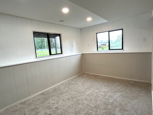 empty room with healthy amount of natural light, carpet, wood walls, and recessed lighting
