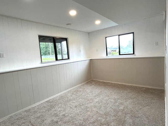 carpeted empty room featuring healthy amount of natural light and wooden walls