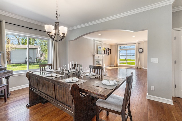 dining room featuring arched walkways, hardwood / wood-style flooring, crown molding, a chandelier, and baseboards