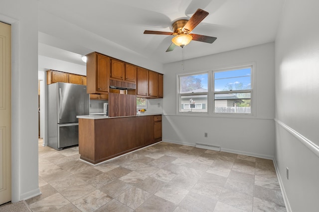 kitchen with freestanding refrigerator, a ceiling fan, brown cabinets, a peninsula, and baseboards