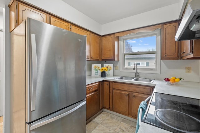 kitchen featuring freestanding refrigerator, a sink, range hood, light countertops, and brown cabinetry