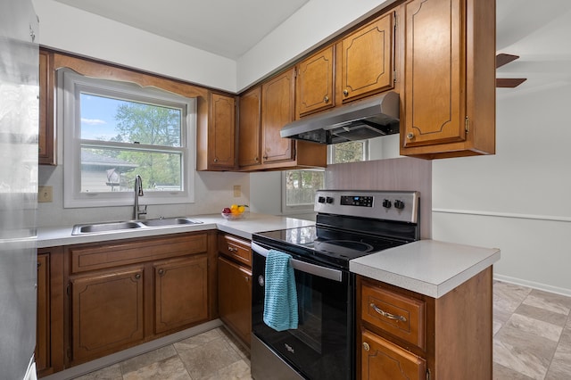 kitchen with stainless steel electric range oven, under cabinet range hood, a sink, brown cabinetry, and light countertops