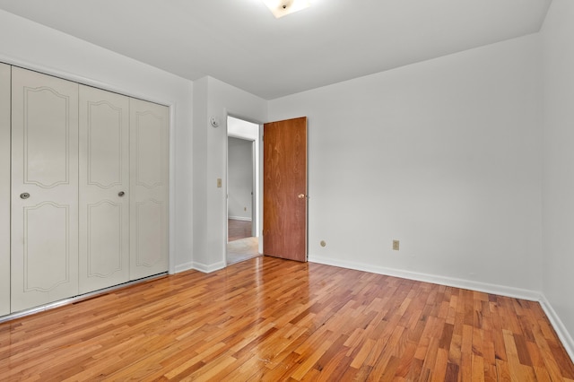 unfurnished bedroom featuring light wood finished floors, baseboards, and a closet