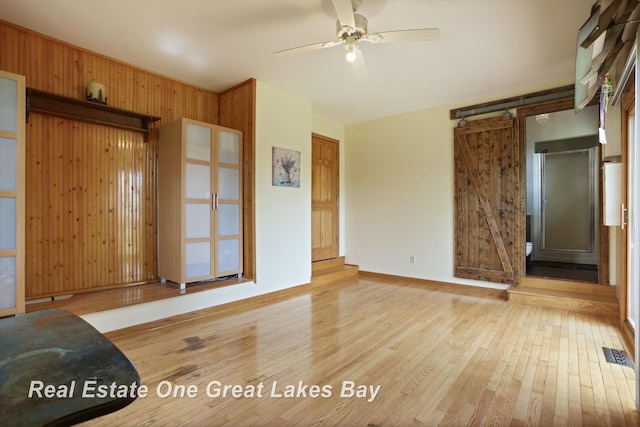 unfurnished living room featuring hardwood / wood-style flooring, ceiling fan, wooden walls, and baseboards