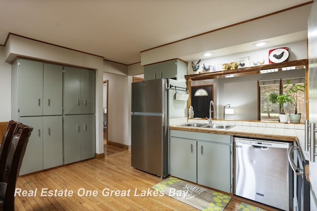 kitchen with stainless steel appliances, a sink, light wood-type flooring, open shelves, and tile countertops