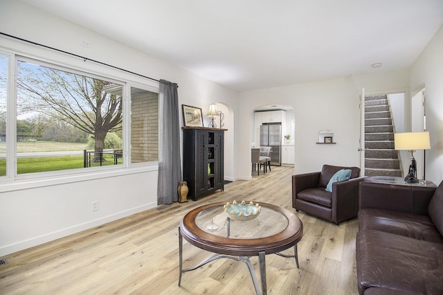 living area with arched walkways, wood finished floors, baseboards, and stairs