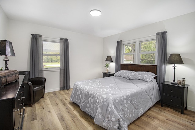 bedroom with multiple windows, light wood finished floors, and baseboards