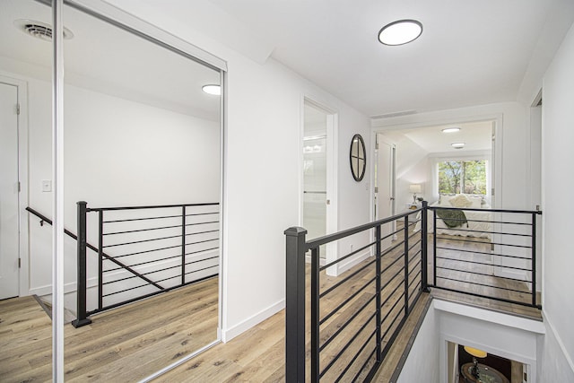 hall with an upstairs landing, wood finished floors, and recessed lighting