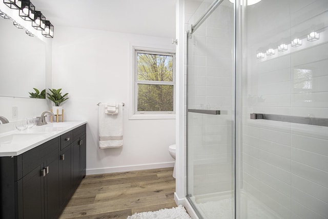 bathroom featuring wood finished floors, a stall shower, double vanity, baseboards, and toilet
