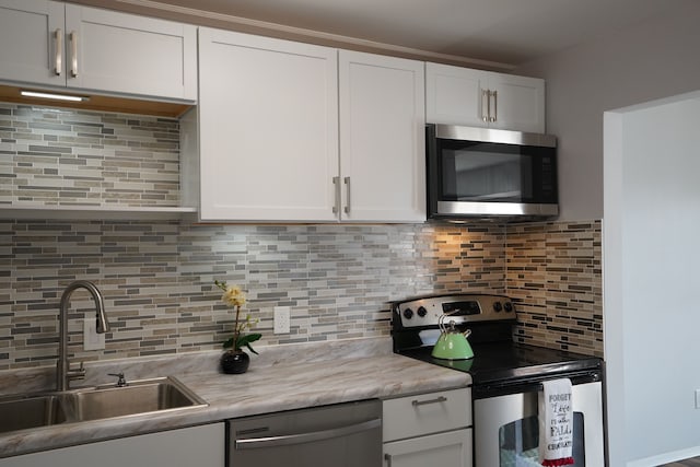 kitchen with stainless steel appliances, a sink, tasteful backsplash, and white cabinets
