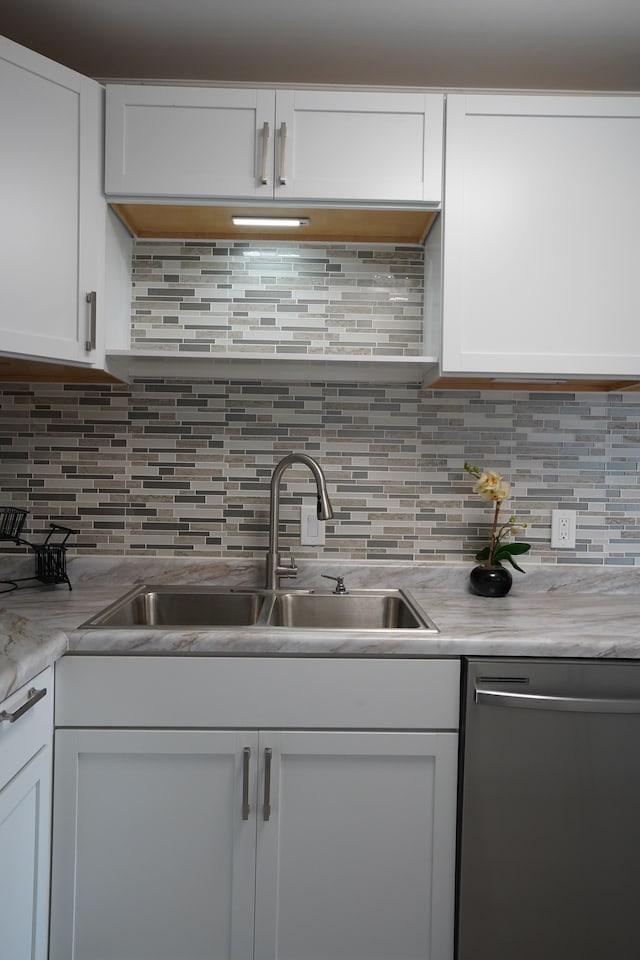kitchen with stainless steel dishwasher, a sink, white cabinets, and light countertops
