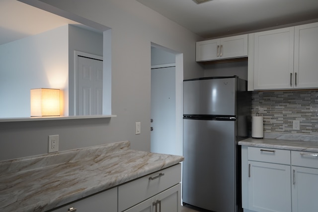 kitchen with freestanding refrigerator, tasteful backsplash, and white cabinetry
