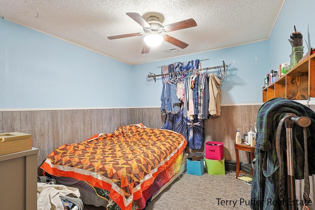 bedroom with a wainscoted wall, wood walls, a textured ceiling, and ceiling fan