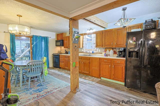 kitchen with black appliances, a chandelier, light wood-type flooring, light countertops, and a sink