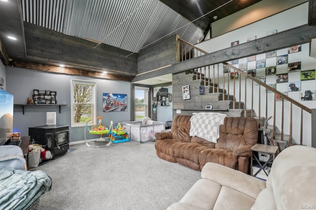 living area featuring a high ceiling, a wood stove, stairs, carpet, and baseboards