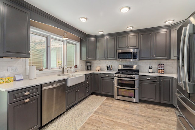 kitchen with stainless steel appliances, a sink, decorative backsplash, and light wood-style flooring