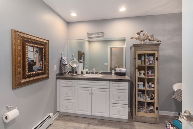 bathroom with vanity, wood finished floors, baseboards, recessed lighting, and a baseboard heating unit