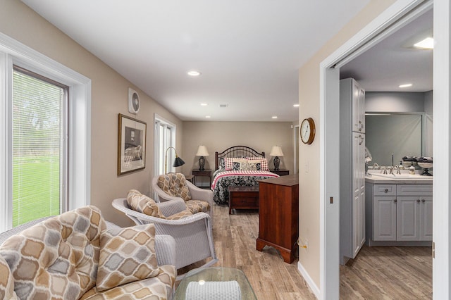 bedroom with light wood-type flooring, multiple windows, a sink, recessed lighting, and ensuite bathroom