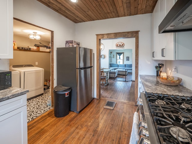 kitchen with appliances with stainless steel finishes, wall chimney exhaust hood, independent washer and dryer, wood-type flooring, and white cabinetry