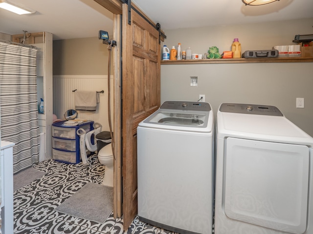 clothes washing area featuring washing machine and dryer, a barn door, and a wainscoted wall