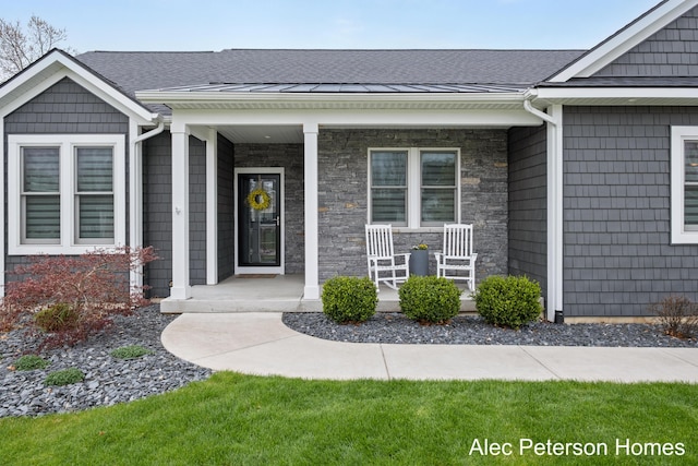 doorway to property with covered porch, roof with shingles, and stone siding