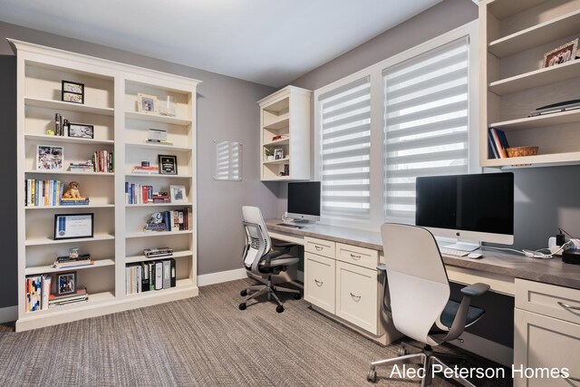 office space featuring carpet flooring, built in desk, and baseboards