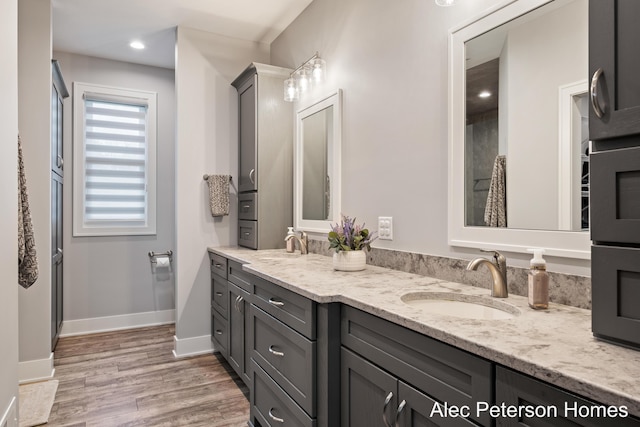 full bath featuring wood finished floors, double vanity, and baseboards