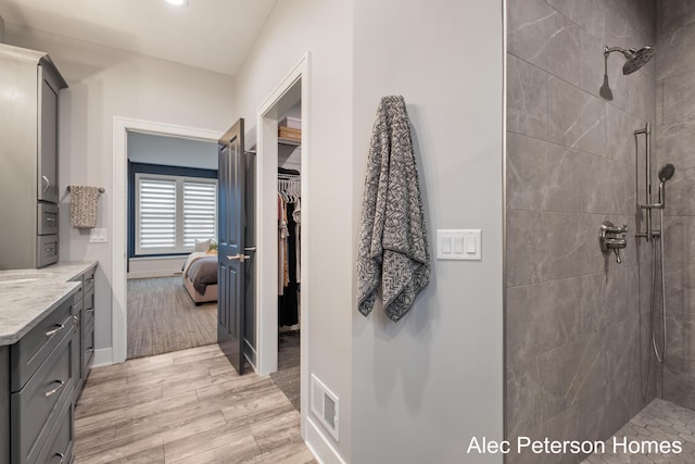bathroom with tiled shower, vanity, wood finished floors, baseboards, and a walk in closet