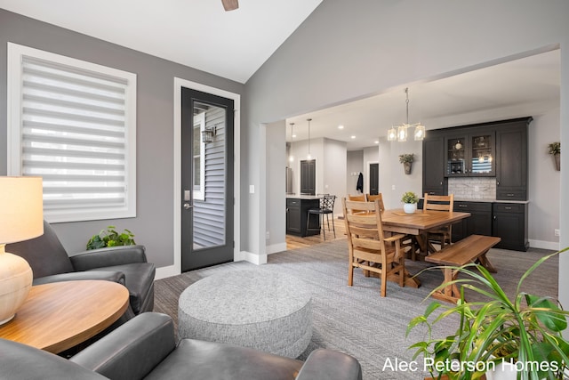 dining area featuring a chandelier, baseboards, light colored carpet, and high vaulted ceiling