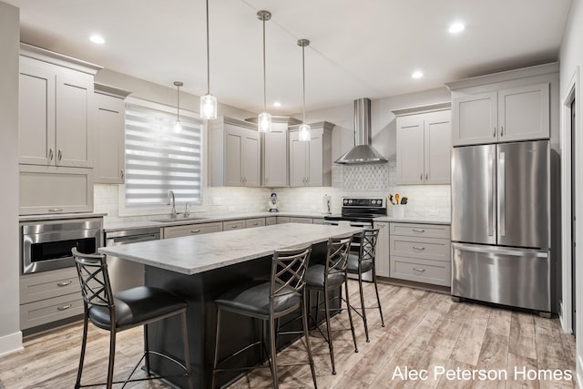 kitchen featuring appliances with stainless steel finishes, wall chimney exhaust hood, a sink, a kitchen breakfast bar, and tasteful backsplash